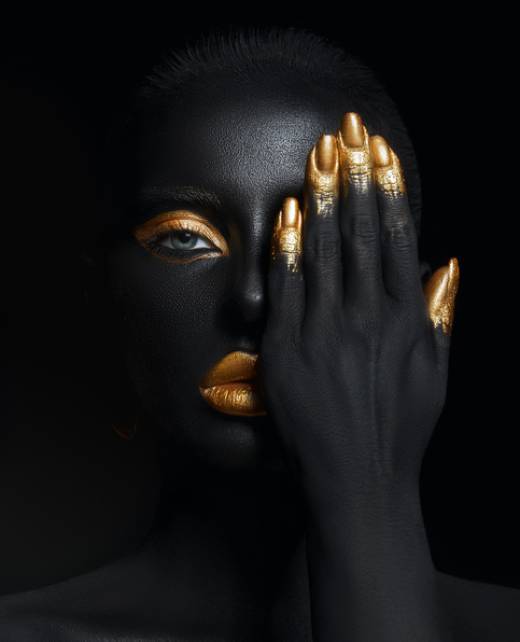 Beauty woman painted in black skin color body art, gold makeup lips eyelids, fingertips nails in gold color paint. Professional gold makeup
